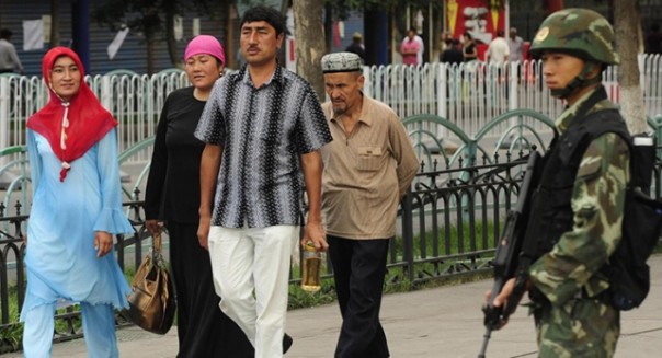 Etnis muslim Uighur berjalan di depan militer China yang berjaga-jaga dengan senjata lengkap. Foto: int 